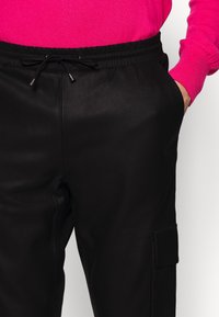 Zwarte joggingsbroek met een gladde textuur, elastische tailleband, een trekkoord met metalen punten en een zijzak met klepdetail.