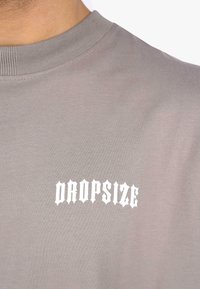 Grå bomulds-t-shirt med ribbet rund hals og teksten "DROPSIZE" i hvid gotisk skrifttype på fronten.