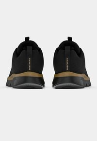 Schwarze Sportschuhe mit einer strukturierten Oberseite, Gummisohlen und einem goldenen Akzent an der Ferse, ausgestattet mit einer Zuglasche auf der Rückseite.