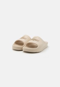 Sandale slip-on bej din cauciuc, cu un design cu vârful deschis. Prezintă un logo de crocodil embossat și o talpă interioară texturată pentru aderență.