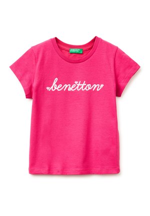 Jasnoróżowy T-shirt z krótkim rękawem, z białym tekstem "benetton" pisanym kursywą na przodzie oraz zieloną metką wewnątrz kołnierza.