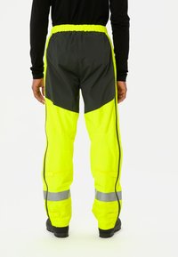Pantaloni impermeabili ad alta visibilità, giallo neon con dettagli neri, vita elastica, strisce laterali e strisce riflettenti all'altezza delle gambe.