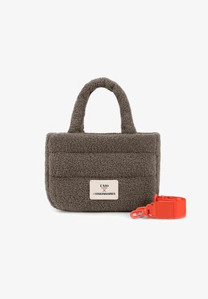 Kleine rechthoekige bruine sherpa handtas met twee handvatten en een wit label, naast een losgemaakt feloranje schouderriem met clips.