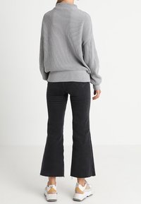 Pull gris côtelé avec un col montant, coupe décontractée et épaules tombantes, associé à un jean noir évasé et des baskets blanches avec des accents jaunes.