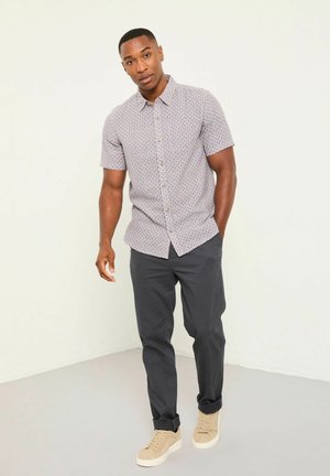 Kurzärmliges Hemd mit Knopfleiste und hellfarbenem Blumenmuster, kombiniert mit dunkler Hose und beigen Turnschuhen. Glatte Stoffstruktur.