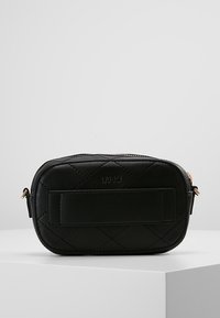 Musta tikattu nahkalaukku pyöreällä muodolla, jossa on vetoketjusuljenta ja tasainen etupaneeli. Kullansävyiset metalliosat näkyvissä.