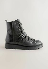 Fekete katonai bakancs sima és texturált bőrből. Fém szemekkel, fűzővel és oldalsó csatolással rendelkezik. Masszív gumi talp.