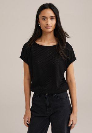 Blusa nera a maniche corte con motivo a zigzag, scollo rotondo e vestibilità rilassata. Abbinata a jeans scuri a vita alta.