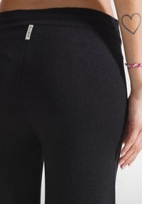 Zwarte gebreide broek met een brede geribbelde tailleband, voorzien van een klein stoffen etiket op de achterkant. Gladde textuur en aansluitend ontwerp.