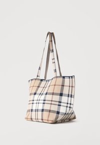 Μπεζ τσάντα ώμου με μακριά χερούλια, διακοσμημένη με κλασικό καρό μοτίβο σε μαύρο, λευκό και καφέ, τοποθετημένη σε απλό φόντο.