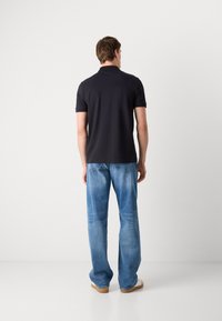 Camisa polo preta de mangas curtas, combinada com jeans de ganga azul clara. Os jeans têm um corte descontraído e desbotamento suave, usados com sapatos bejes.