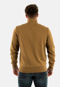 Sudadera marrón con cremallera y cuello alto, puños y cintura de canalé, textura suave y corte ajustado, mostrada desde la parte posterior.