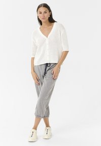 White knitted cardigan with short sleeves and buttons, paired with striped cropped pants. White sneakers complete the outfit.
