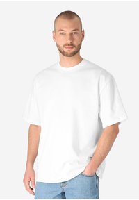 White cotton t-shirt with short sleeves and a crew neckline, displayed on a person wearing light blue jeans, set against a plain background.