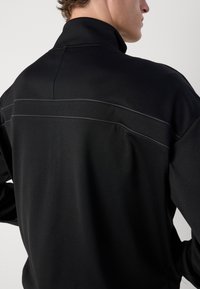 Pullover preto com gola alta, apresentando acabamentos em cinza contrastante na parte de trás. Feito em tecido suave com um corte justo.