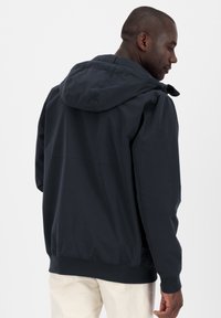 Giacca a vento navy con cappuccio realizzata in tessuto leggero, dotata di polsini e bordo elastici. Caratterizzata da una vestibilità comoda, cuciture a vista e un design minimal.