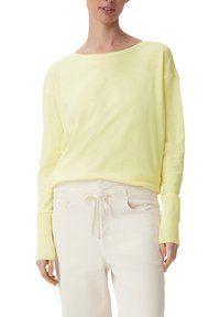 Ljusgul stickad tröja med vid halsringning och långa ärmar, kombinerad med beiga byxor med dragsko. Slät textur, avslappnad design.