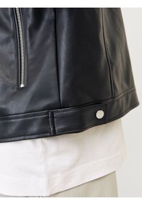 Czarna skórzana kurtka z metalowym suwakem po stronie oraz zatrzaskiem u dołu. Materiał ma gładką fakturę z minimalną ilością szwów.