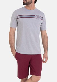 T-shirt gris à manches courtes avec des rayures horizontales bordeaux et bleues et un patch logo circulaire. Assorti avec un short bordeaux. Tissu en mélange de coton.