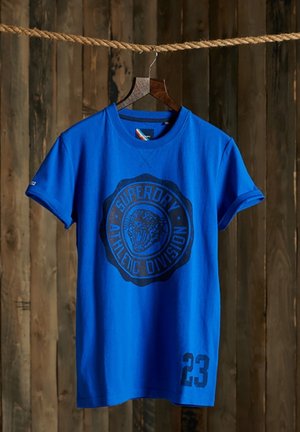 Sininen puuvillainen t-paita pyöreällä pääntiellä, jossa on musta pyöreä graafinen painatus ja numero "23" vasemman etureunan alareunassa.