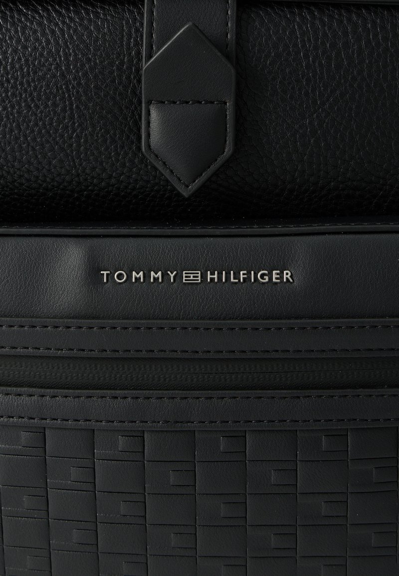 Black leather shoulder bag featuring textured surface, geometric pattern, and silver logo detailing. The design is sleek and compact.