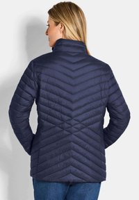 Marineblauwe geïsoleerde jas met een chevron-quiltpatroon en hoge kraag. Het materiaal lijkt glad en heeft een lichtgewicht ontwerp.