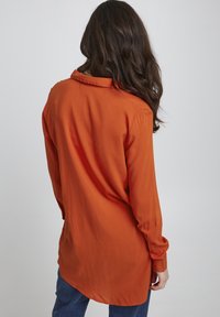 Langärmliges Hemd in leuchtendem Orange, mit klassischem Kragen und glatter Textur. Der Rücken hat einen abgerundeten Saum und einen lässigen Schnitt.