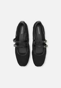 Des chaussures noires à enfiler avec une tige en maille texturée, deux sangles noires avec des boucles en métal argenté, et un design à bout rond.