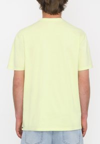 Camiseta de algodón color amarillo claro con escote redondo, mangas cortas y dobladillo recto. Diseño liso sin patrones ni acentos visibles.