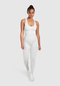Monosuit blanco ajustado al cuerpo con escote redondo y tirantes finos, hecho de tela suave; combinado con zapatillas deportivas blancas.