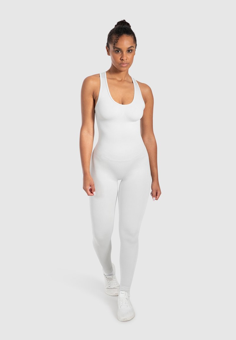 Monosuit blanco ajustado al cuerpo con escote redondo y tirantes finos, hecho de tela suave; combinado con zapatillas deportivas blancas.