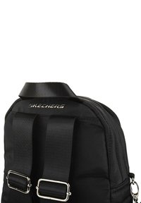Mochila negra de nailon con textura acolchada, correas ajustables, acentos de hardware plateado y un logotipo de marca prominente en la parte superior.