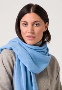 Sciarpa in cashmere azzurro chiaro avvolta attorno a un cappotto grigio, caratterizzata da una morbida texture e una caduta rilassata. Tessuto liscio e leggero.