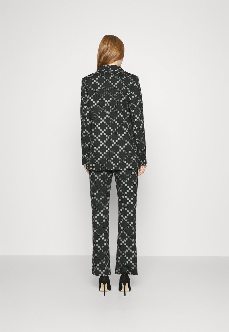Completo a righe in bianco e nero con giacca su misura e pantaloni a zampa. Il materiale appare lucido; presenta un design geometrico distintivo e revers pronunciati.