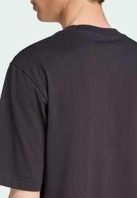 Sort bomulds T-shirt med rund halsudskæring, der har korte ærmer og en glat tekstur, vist fra ryggen, med fokus på skuldersømmen.