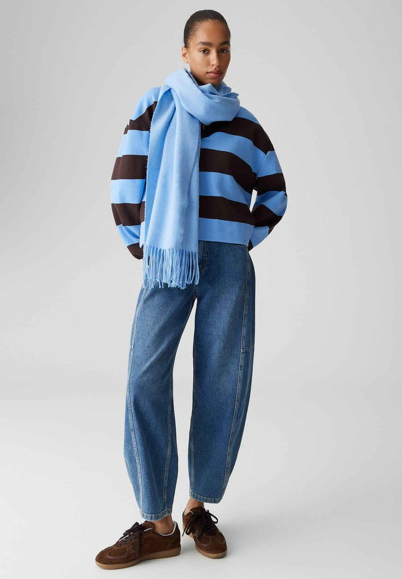 Pull rayé bleu et marron, écharpe bleu clair, jean taille haute en denim et baskets marron. Écharpe à franges, coupe décontractée.