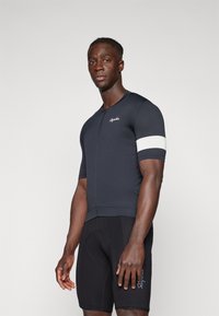 Maillot de cyclisme marine avec une courte fermeture éclair et une bande blanche sur la manche, associé à un short noir rembourré, tous deux en tissu texturé.
