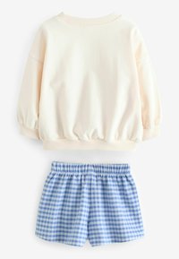 Pullover crema con maniche a palloncino e scollatura a costine; abbinato a pantaloni corti a quadri blu e bianchi, con fascia elastica in vita.