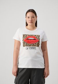 T-shirt en coton blanc avec un design graphique de lèvres rouges sur un fond imprimé léopard, avec le texte "LA FEMME" en dessous. Manches courtes.