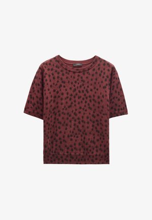 Krótki rękaw, bordowy sweter z czarnym nieregularnym wzorem w kropki, okrągły dekolt oraz ściągacze przy mankietach i u dołu.