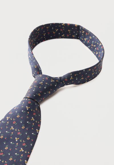 Στενή γραβάτα σε ναυτικό μπλε με μικρά λουλουδένια και μελισσένια σχέδια, χαλαρά δεμένη και τοποθετημένη σε λευκό φόντο.