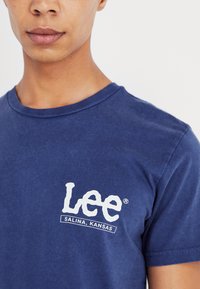 Granatowa bawełniana koszulka z białym logo "Lee" z napisem "Salina, Kansas" poniżej, okrągłym dekoltem i krótkimi rękawami.