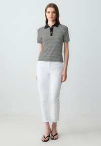 Polo a righe bianche e nere con colletto nero a tinta unita, abbinato a jeans bianchi slim-fit e ciabatte nere.