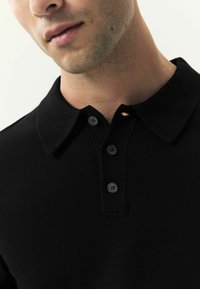 Mustmustelne polo-särk ribaga kraega ja kolme musta nupuga, millel on sile kangatekstuuri ja klassikaline disain.