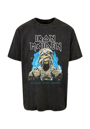 Fekete pamut póló, amelyen egy kötözött és lánccal körülvett koponya grafika látható, kék villámló elemekkel, valamint az "Iron Maiden World Tour 1984-85" felirattal.