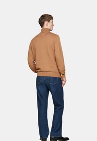 Brauner Strickpullover mit hohem Kragen, schmalen Bündchen und glatter Textur, kombiniert mit dunkelblauen geraden Jeans und schwarzen Schuhen.