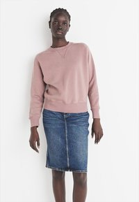 Sweatshirt rose clair avec encolure ras du cou et poignets côtelés, associé à une jupe crayon en denim bleu avec une couture avant et un ourlet.