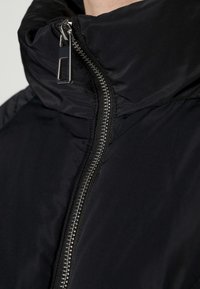 Svart puffjacka med hög krage, med en silverdragkedja, slät textur och en ren, minimalistisk design.