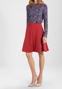 Top floral de manga larga con escote redondo en azul oscuro y flores multicolores, combinado con una falda roja plisada y tacones rosa claro.