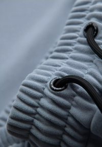 Tissu de vêtement bleu clair avec des stries texturées et un cordon noir. Comprend une étiquette circulaire noire avec "comple" imprimé dessus.